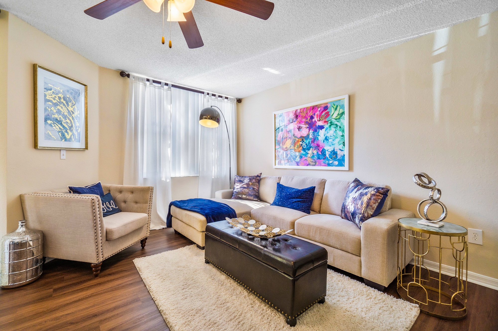 A living room with a beige couch, a chair, a coffee table, and a painting on the wall.